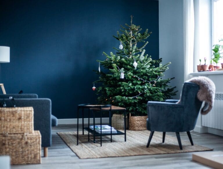 Christmas tree in the interior. Scandinavian style, minimalism. Dark blue wall, grey chair, braided baskets. White paper origami toys.