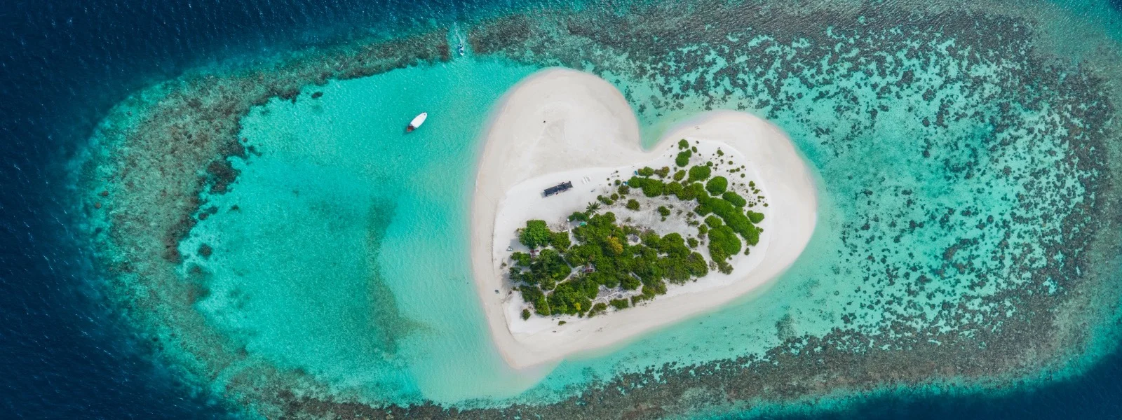 Drone Aerial view of beautiful tropical heart shaped island among blue sea water at Maldives paradise with boat on background